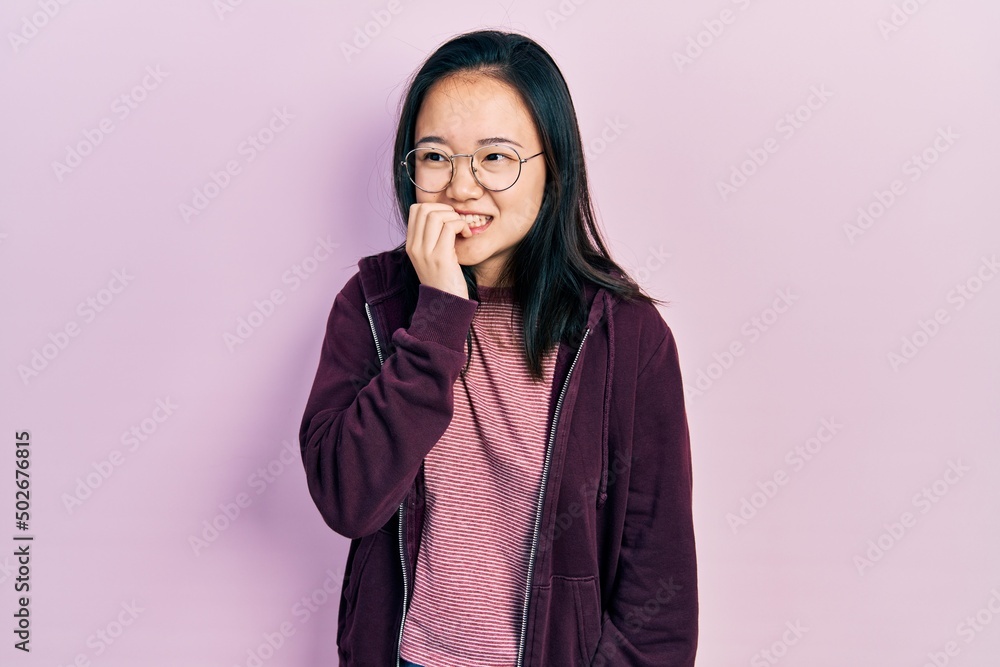 Young chinese girl wearing casual clothes and glasses looking stressed and nervous with hands on mouth biting nails. anxiety problem. Young chinese girl wearing casual clothes and glasses looking stressed and nervous with hands on mouth biting nails. anxiety problem.