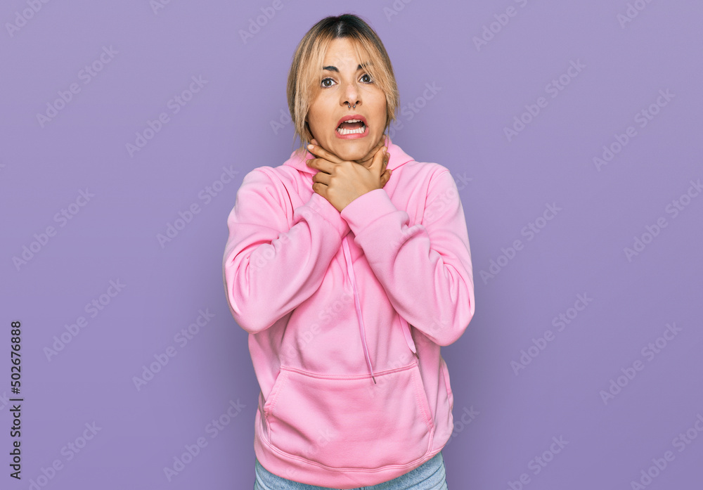 Fototapeta premium Young caucasian woman wearing casual sweatshirt shouting and suffocate because painful strangle. health problem. asphyxiate and suicide concept.