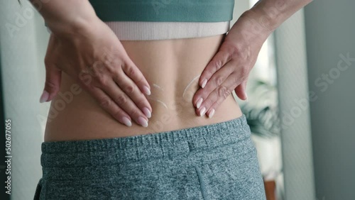 Woman rubs pain relief ointment into low back while wearing active clothing