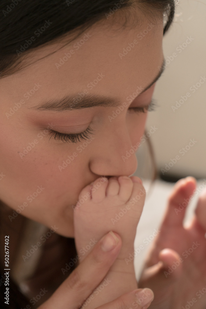Latin young mother kisses baby feet and sniff them on the bed at home Latin young mother kisses baby feet and sniff them on the bed at home