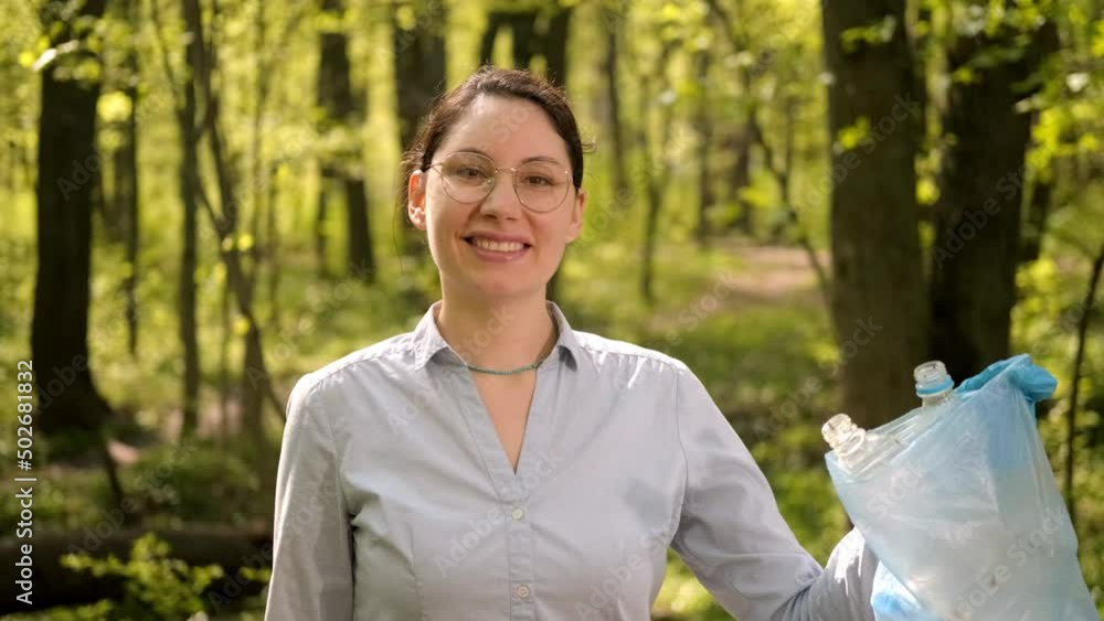 A young brunette woman with glasses ecologist puts garbage in a bag. Forest cleaning. Careful treatment of nature. Cleaning day A young brunette woman with glasses ecologist puts garbage in a bag. Forest cleaning. Careful treatment of nature. Cleaning day
