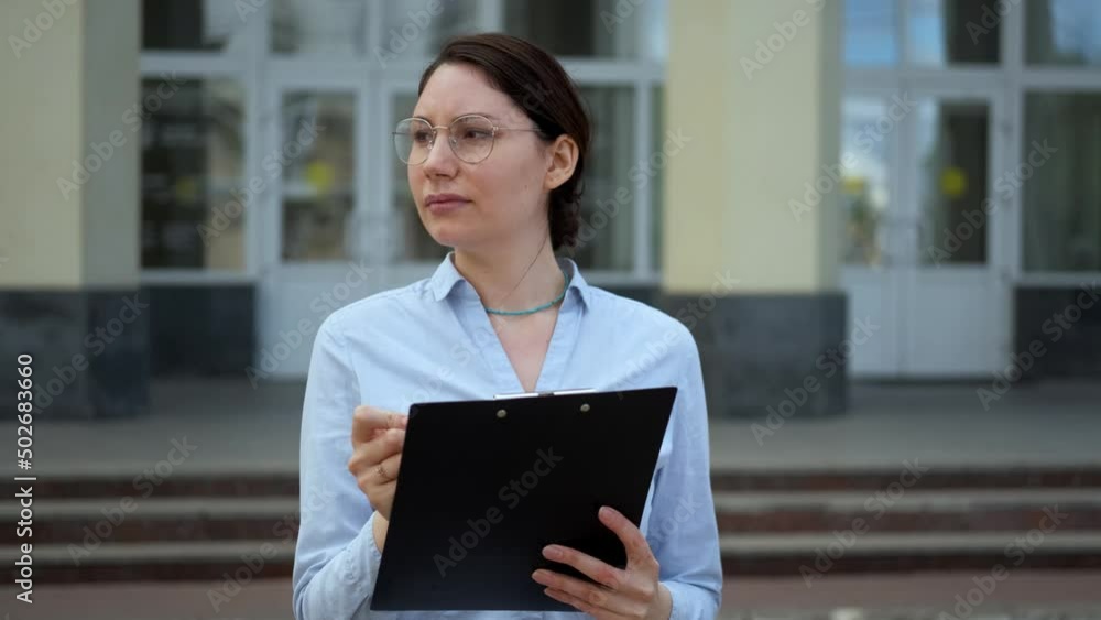 A beautiful brunette girl student with glasses makes notes on the background of the university. Education and science A beautiful brunette girl student with glasses makes notes on the background of the university. Education and science
