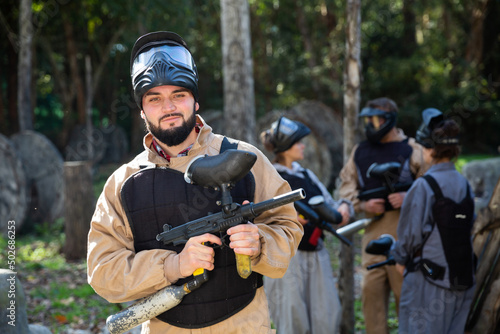 Man paintball player in camouflage standing with gun before playing outdoors