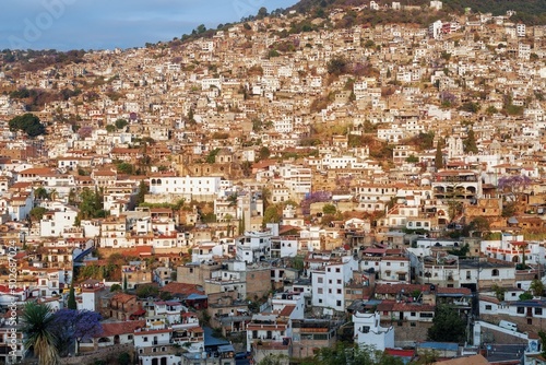 The city is illuminated by the sun in the morning on a mountainside with colonial architecture, many white houses with tiles. The cramped streets of Taxco in Mexico