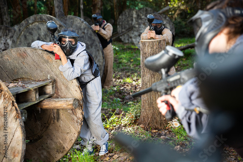 Excited male and female paintball players in protective uniform aiming and shooting with guns