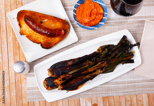 Traditional dishes of Catalonia, calcot with romesco sauce and grilled botifarra sausage served on table. photo