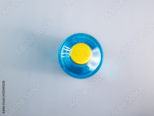 Bottle of ethyl alcohol solutions 70 percent taken from above. It's a golden yellow cap. A light blue liquid with reflections on a gray background.