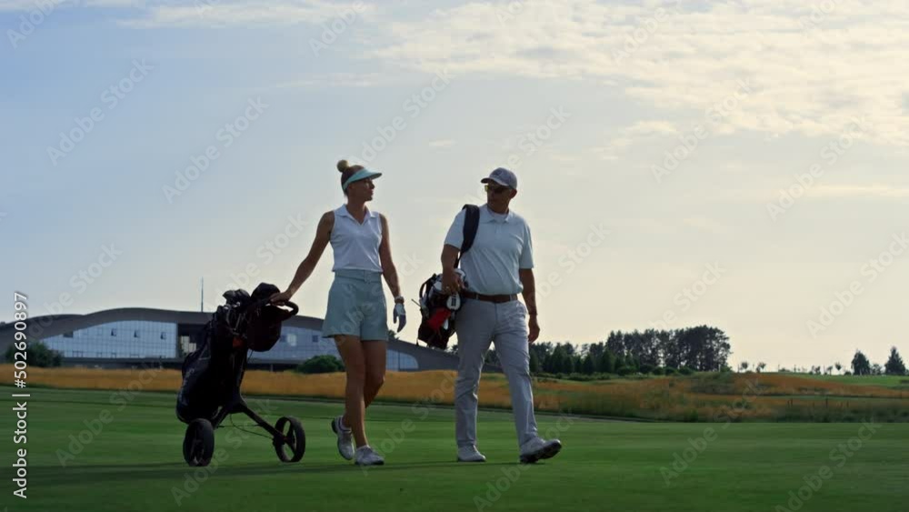 Couple golf players discuss sport course outside. Two golfers walk grass field. Couple golf players discuss sport course outside. Two golfers walk grass field.