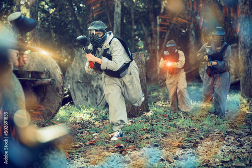 Adult paintball players of opposite teams playing in shootout outdoors, image with light effects