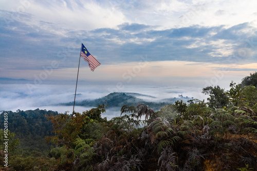 Malaysia flag flying on pole on mountain highland against sea of cloud and blue sky