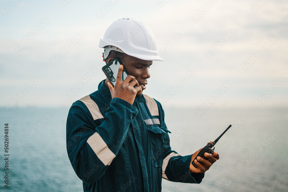 Black seaman with walkie talkie speaking on smartphone Black seaman with walkie talkie speaking on smartphone