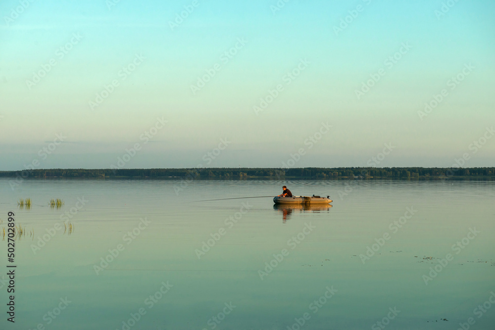 The boat floats on the calm blue water of the lake. fishermen set sail early in the morning for fishing. silence and grace, photos in blue tones, a panarama of a lake view. copy space.