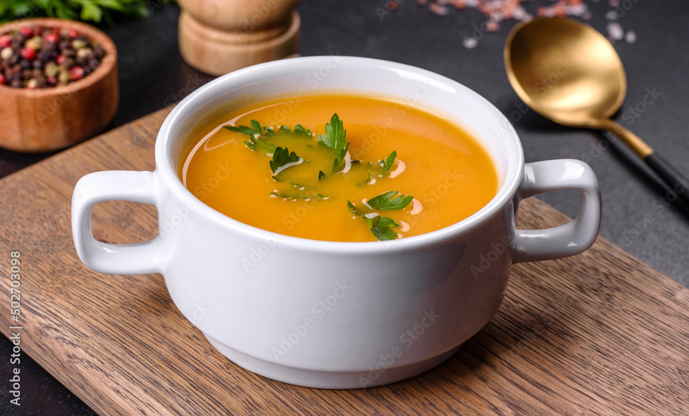 Delicious fresh pumpkin puree soup decorated with parsley in a white plate Delicious fresh pumpkin puree soup decorated with parsley in a white plate