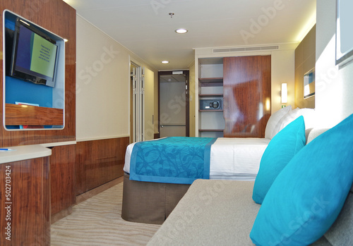 Balcony veranda bedroom stateroom cabin suite in clean modern interior design onboard luxury cruiseship cruise ship liner with pillows, duvet blanket, couch and wooden closets