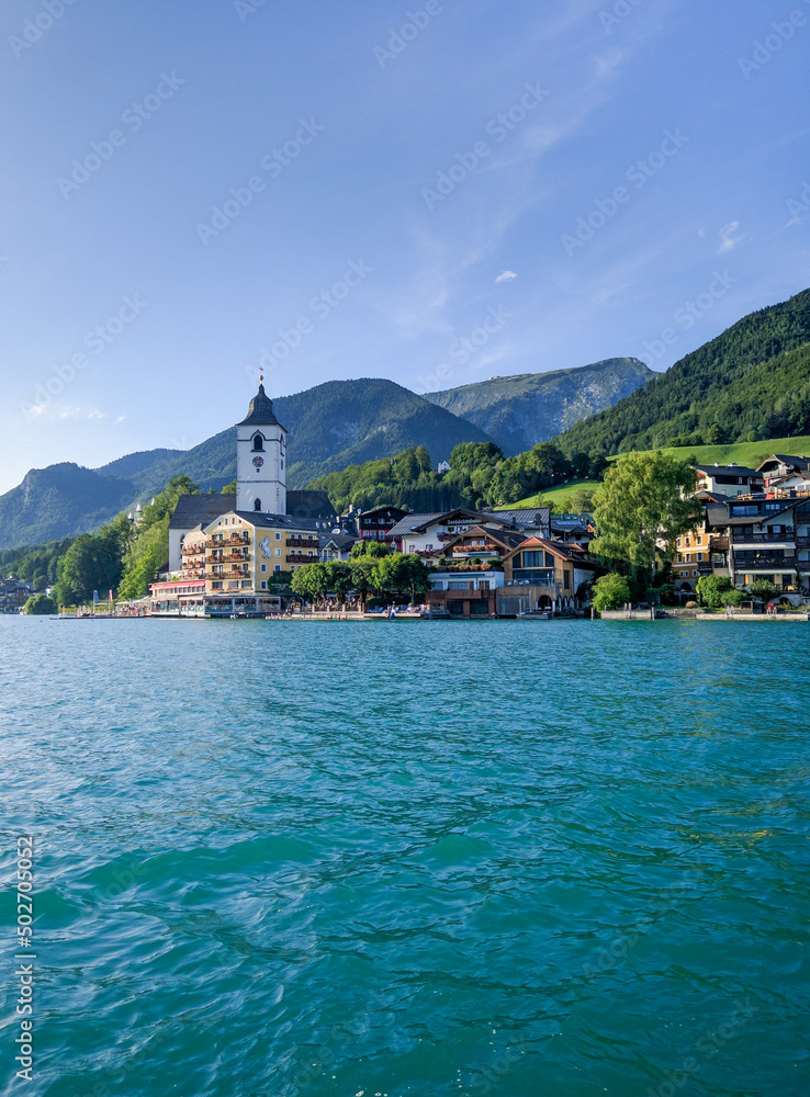 St. Wolfgang, Austria - August 16, 2019: Beautiful view from the lake to the architecture of the city of St. Wolfgang against the backdrop of the Alps. Church of St. Wolfgang is the main attraction