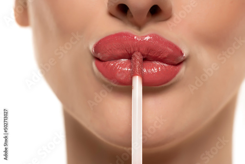 Fototapeta young beautiful woman apply a lip gloss on her lips on white background