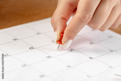 beautiful female Hand with manicure pushes a red pin on a calendar