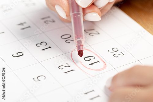 close up on employee woman hand using red pen to writing schedule on 19th day of the monthcalendar 2022 to make an appointment meeting or manage timetable each day at house for work from home concept photo