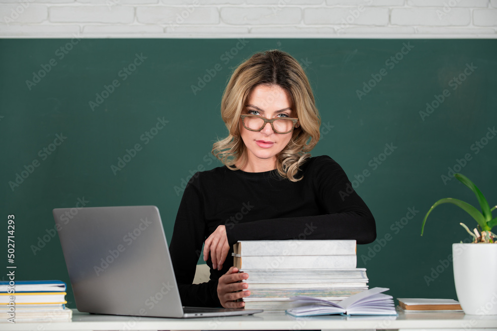 Sensual student woman in eyeglasses near blackboard. Sexy girl sit on table on chalkboard. Sensual student woman in eyeglasses near blackboard. Sexy girl sit on table on chalkboard.