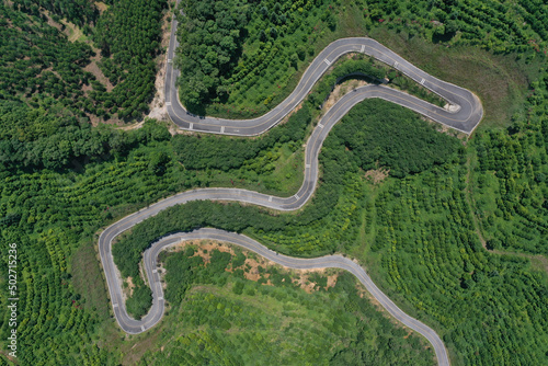 Winding road passes through mountain top forest, aerial top view