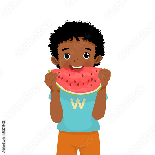 Cute little African boy eating and holding watermelon on sunny day in summertime
