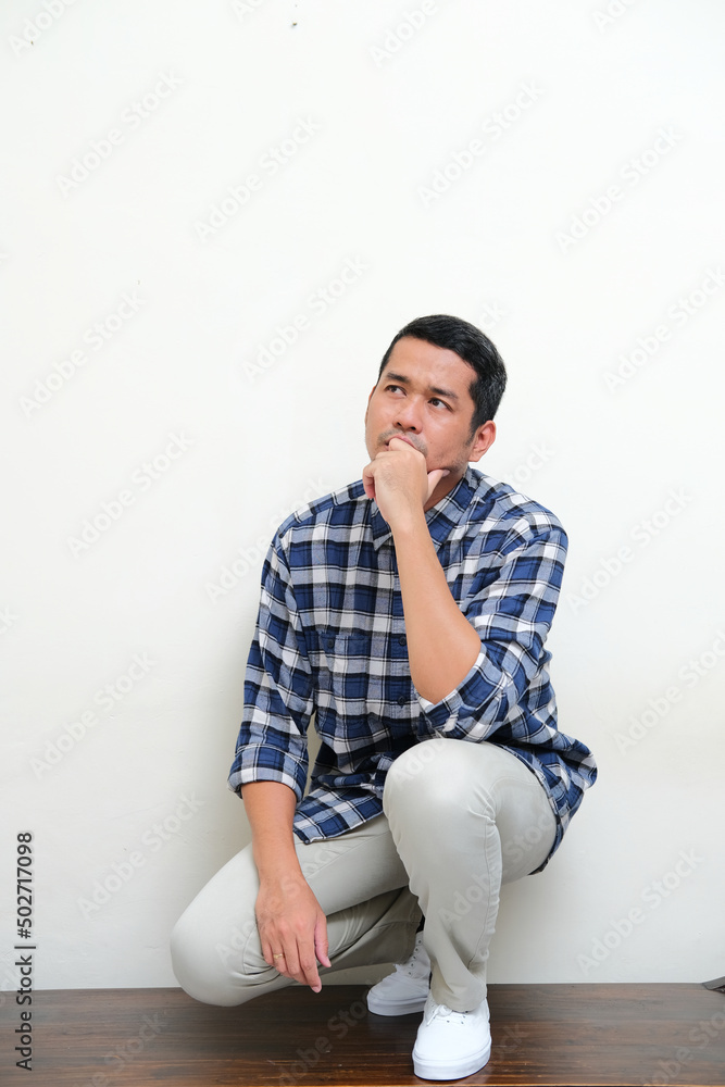 Full body portrait of Adult Asian man showing thinking gesture on knee Full body portrait of Adult Asian man showing thinking gesture on knee