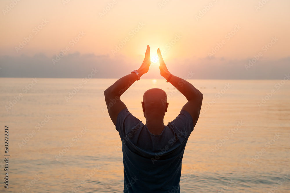 Silhouette man with his hands raised at sunset on beach arms out to sides towards the sun, concept for religion, worship, prayer and praise and success in life, peace and tranquility in nature