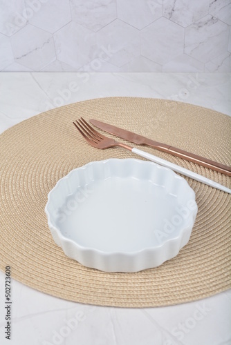 luxury white small dessert plate and rose gold fork, knife and round mat in white marble background for hotel cafe