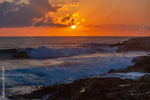 Bright beautiful stunning sea sunset, waves beating against the rocks in the rays of the setting sun © olezzo