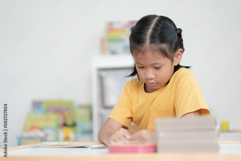 Asian schoolgirl reading book in her room. A kid enjoy reading books alone. Black hair Thai-Chinese girl concentrate reading book by her own. Asian schoolgirl reading book in her room. A kid enjoy reading books alone. Black hair Thai-Chinese girl concentrate reading book by her own.