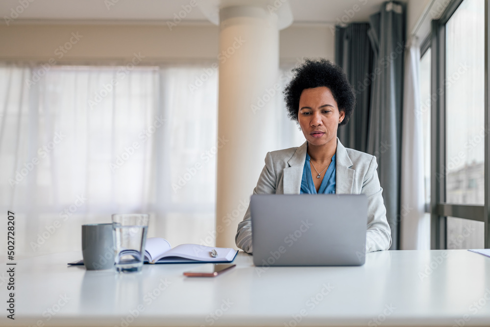 Serious businesswoman using laptop while sitting at desk in corporate workplace Serious businesswoman using laptop while sitting at desk in corporate workplace