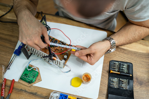 The young master electronics engineer checks, repairs and finishes the motherboard he was given to repair. He uses his tools and works in a home environment.