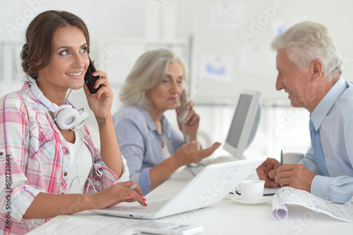 Businesswoman talking on smartphone in modern light office with her colleagues