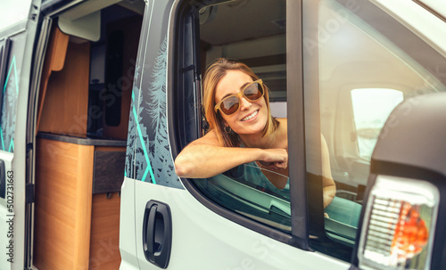 Happy young woman in sunglasses sitting in camper van leaning on the door photo