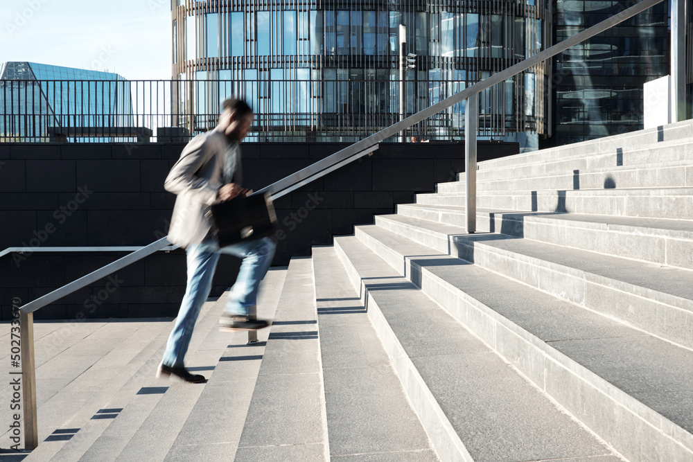 Obraz premium African American white collar worker running up the steps towards modern business center, blurred motion
