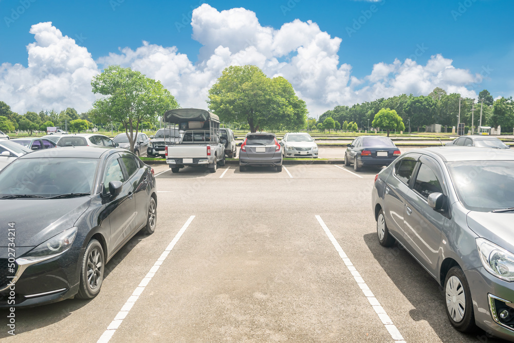 Car parking in asphalt parking lot and empty space parking with trees, white cloud and blue sky background. Outdoor parking lot