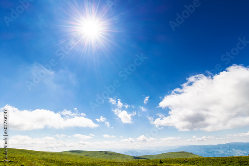 sun shine on the blue sky. white fluffy clouds above the hilly mountain landscape. beautiful nature background on a sunny summer day at high noon © Pellinni