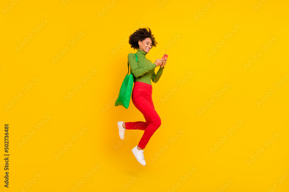 Full size profile side photo of young girl use mobile share repost shopping market jump up isolated over yellow color background