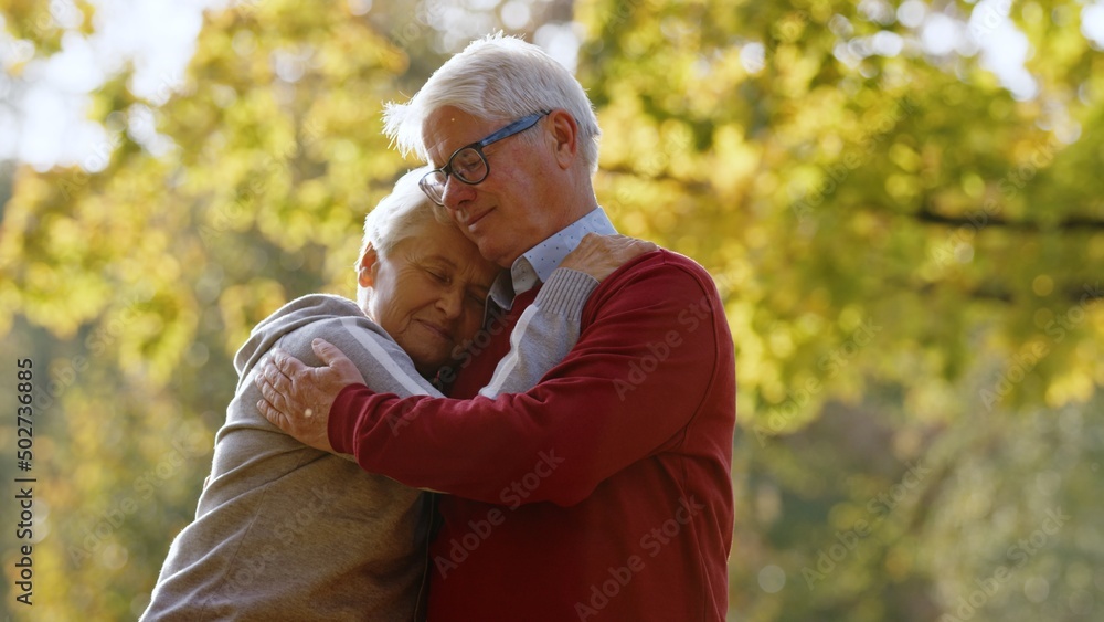 Give me a hug. Embrace between elderly retired caucasian lady and her gray-haired husband in red sweater. True love lasts long. . High quality photo Give me a hug. Embrace between elderly retired caucasian lady and her gray-haired husband in red sweater. True love lasts long. . High quality photo