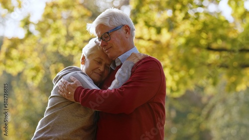 Give me a hug. Embrace between elderly retired caucasian lady and her gray-haired husband in red sweater. True love lasts long. . High quality photo