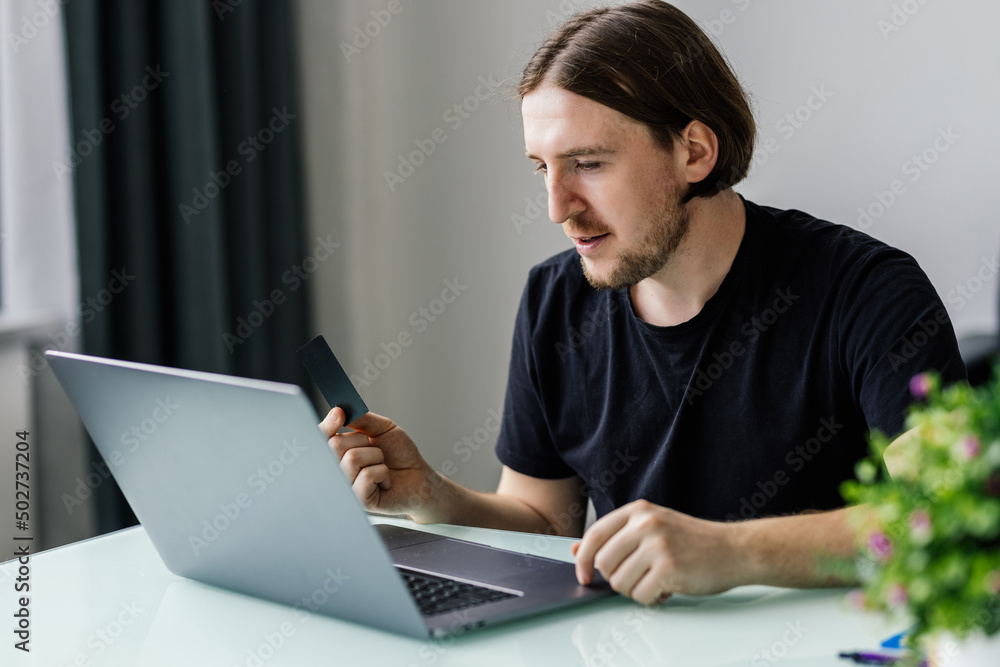 Modern technology, business, career, e-commerce and online trading concept. Businessman holding credit card in one had and keyboarding on laptop with other hand, making transaction Modern technology, business, career, e-commerce and online trading concept. Businessman holding credit card in one had and keyboarding on laptop with other hand, making transaction