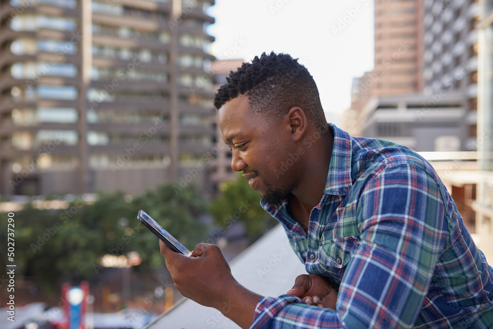 Naklejka premium A Black businessman texts on cellphone during his coffee break on office balcony