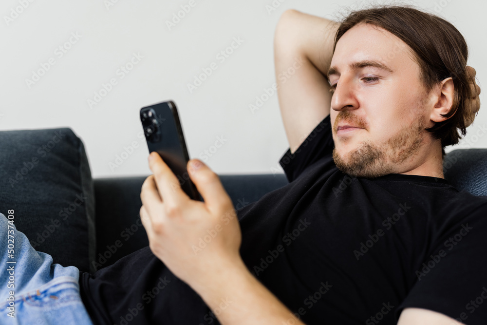 Confident bearded man is sitting on couch and typing on smartphone. Confident bearded man is sitting on couch and typing on smartphone.