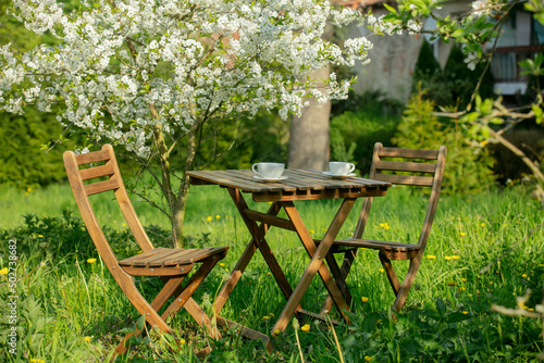 Cup of coffee or tea on wooden table next to blooming tree in a garden