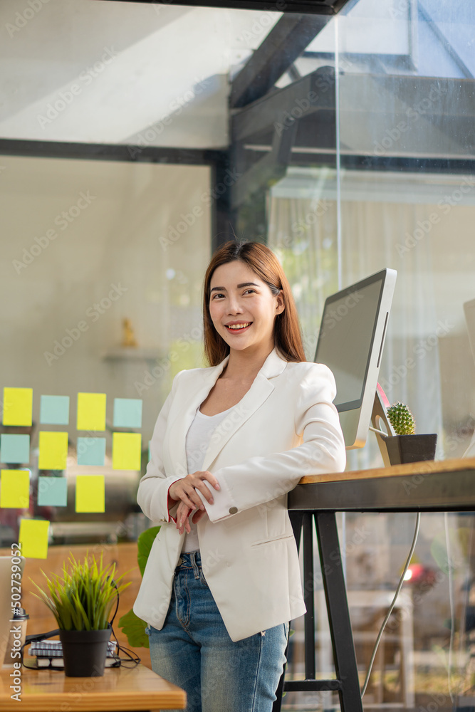 A happy Asian woman in a white dress stands at his desk smirking gleefully at a financially successful business. A happy Asian woman in a white dress stands at his desk smirking gleefully at a financially successful business.