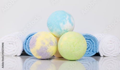 close-up of multicolored bath salts, in the form of bombs and towels wrapped in a roll, on a white table with a reflection