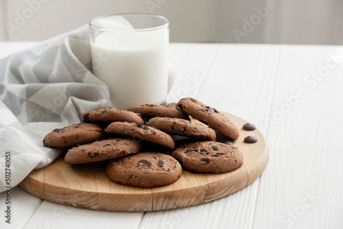 Homemade chocolate chip cookies on wooden board with glass of milk and kitchen towel. Recipe of oatmeal cookies with chocolate chips. Variant of morning breakfast.