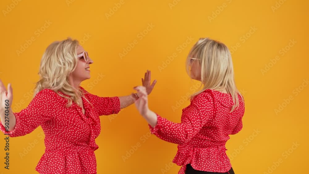 two blonde Caucasian women with sunglasses dancing and enjoying medium shot studio shot orange background well-being concept. High quality 4k footage two blonde Caucasian women with sunglasses dancing and enjoying medium shot studio shot orange background well-being concept. High quality 4k footage