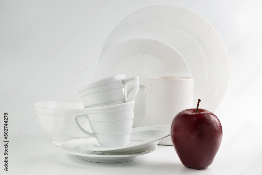 A variety of white tableware on a light background and a burgundy apple. A variety of white tableware on a light background and a burgundy apple.