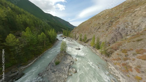 Aerial view fast movement wild water flow mount river with stones narrow gorge surrounded by autumn scenery. FPV sport drone shot picturesque sunny environment waterfall cascade at woodland terrain photo